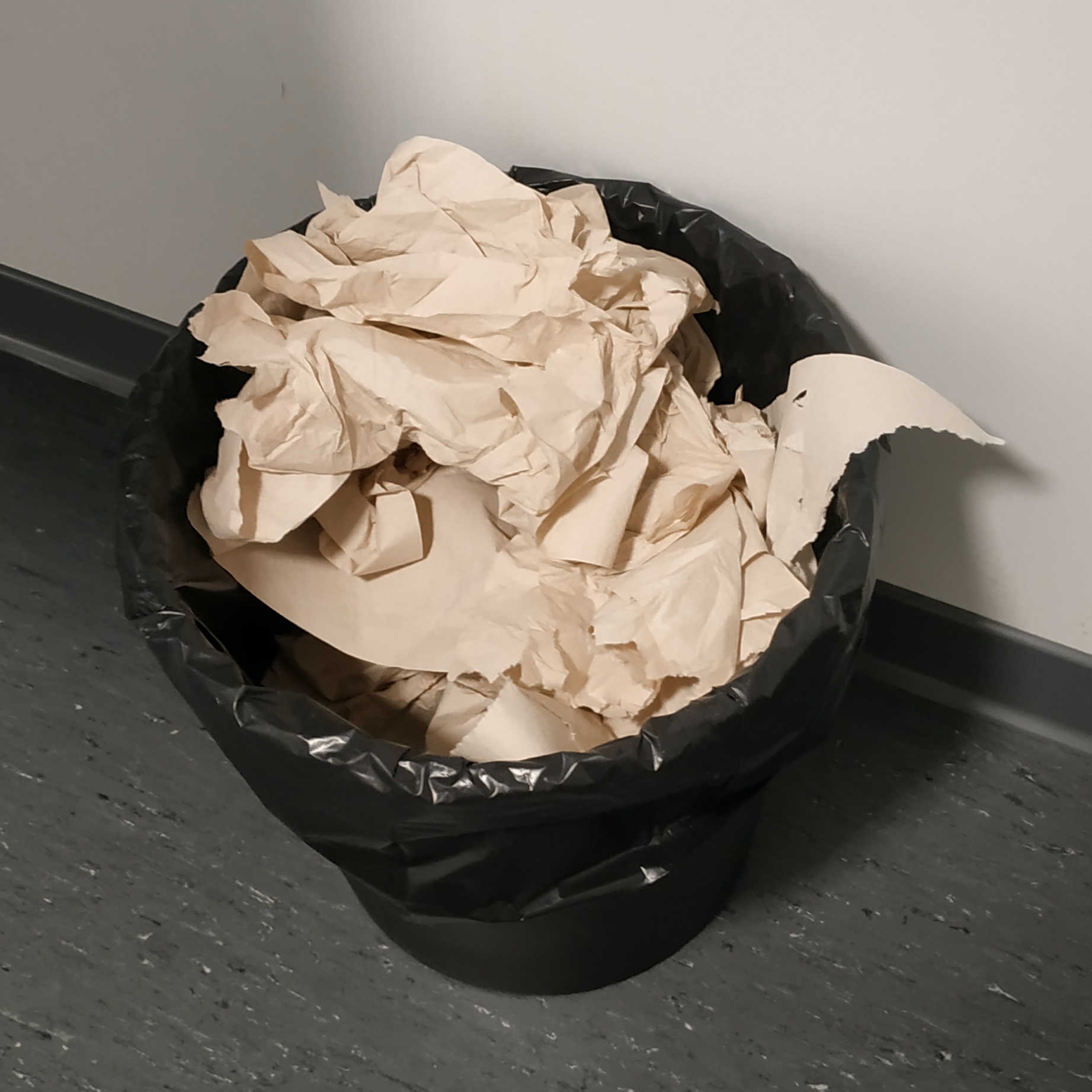 Une poubelle remplie en plongée. On y voit beaucoup de papier et un morceau du lavabo au-dessus de la poubelle.